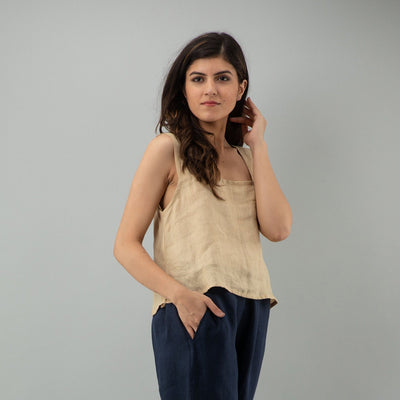 Beige Linen Sleeveless Crop Top: angled pose in Beige crop top, hand raised to hair
