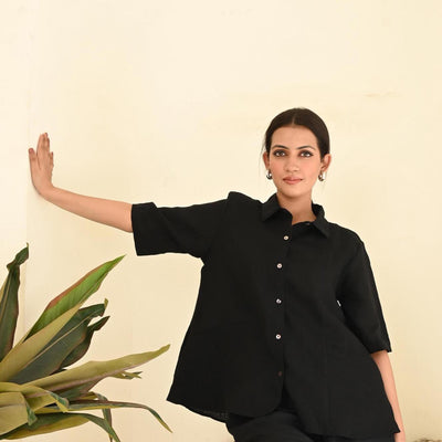 Black Linen Button-Down Shirt, Oversized: arm extended against a wall in Black button-down shirt