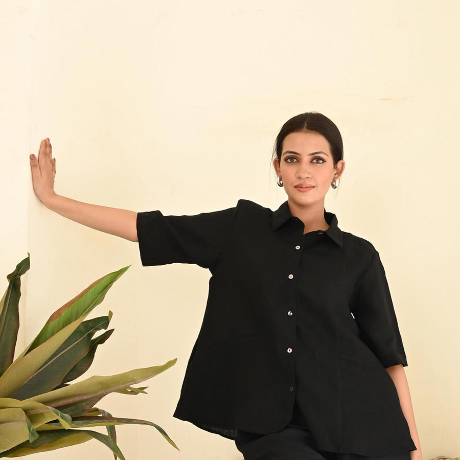 Black Linen Button-Down Shirt, Oversized: arm extended against a wall in Black button-down shirt