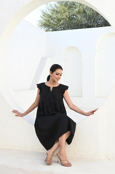 Black Linen Midi Dress with Ruffle Trim: woman in black ruffle linen midi dress seated in an arched doorway