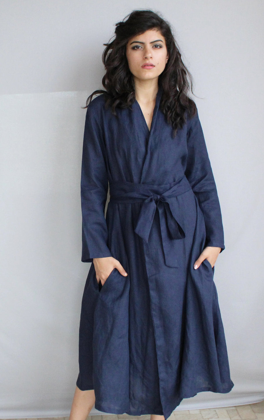 Blue Linen Kimono Wrap Dress: woman in Navy Blue linen kimono wrap dress with tie belt, hands in pockets
