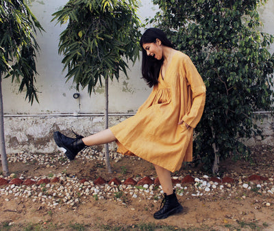 Cottagecore Linen Midi Dress: woman kicking one leg up in mustard linen midi dress and black boots