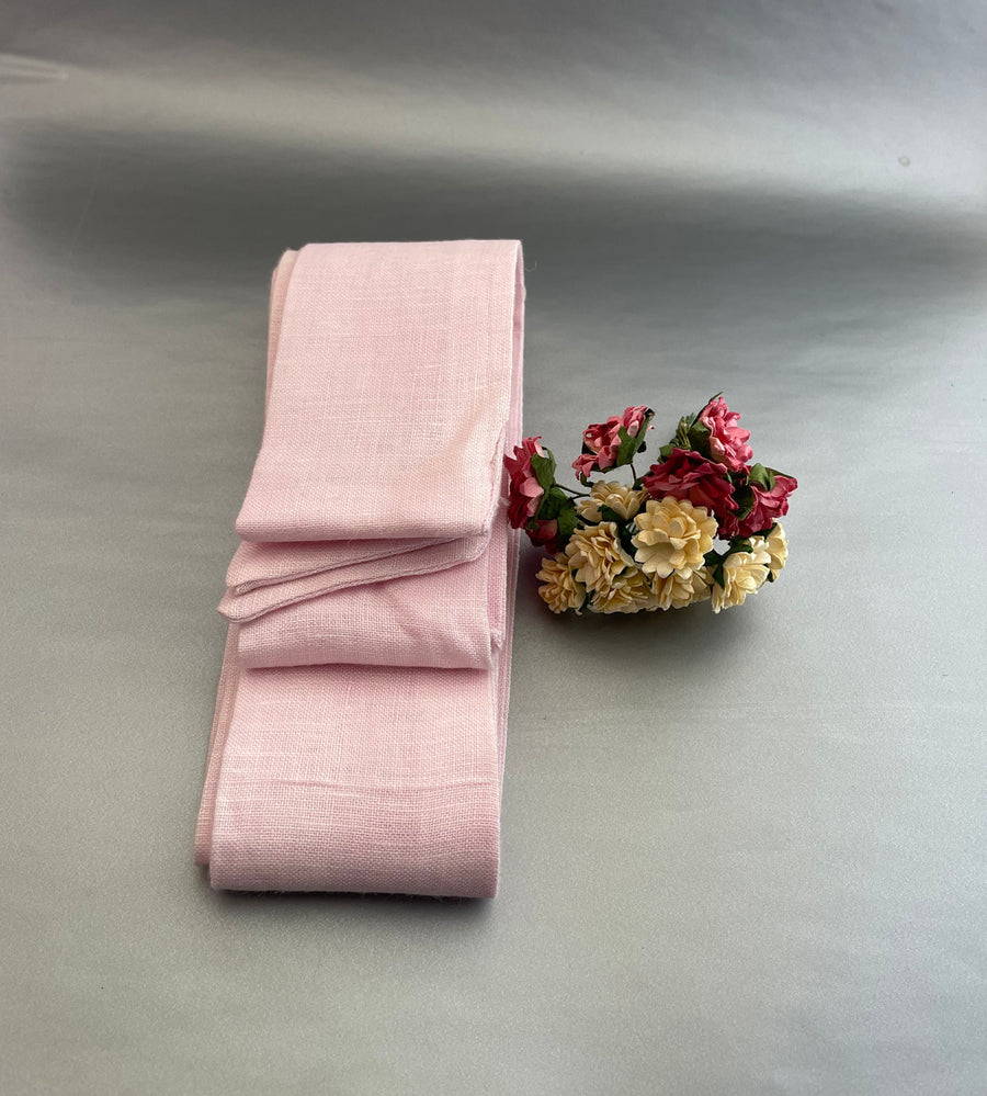 Handmade Linen Belt: Light Pink linen belt folded upright, flowers beside it