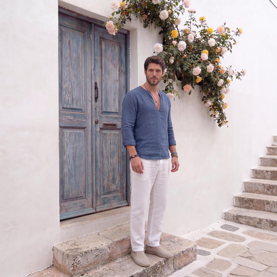 Men's Linen V-Slit Neck Shirt, No Buttons: wide view of man in steel blue linen shirt and white trousers by a blue door
