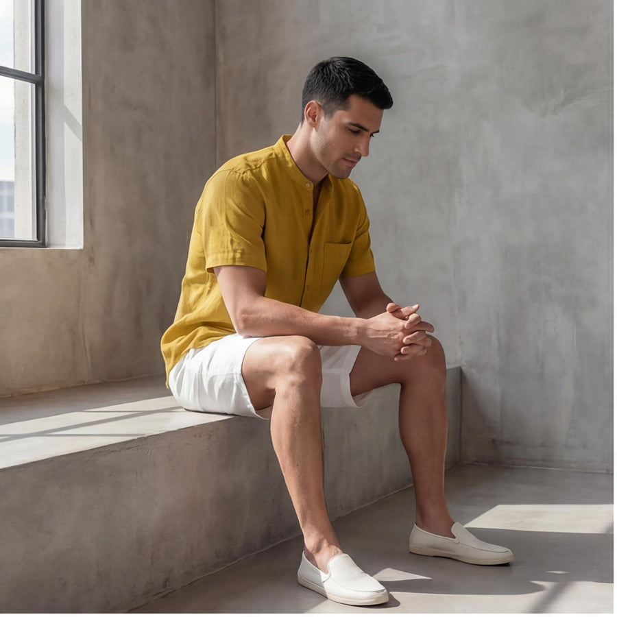 Men's Oversized Short Sleeve Linen Shirt: man seated on a ledge, elbows on knees, mustard shirt