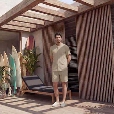 Men's Short Sleeve Linen Shirt, Resort Fit: man in Beige linen shirt and shorts standing by a lounger and surfboards