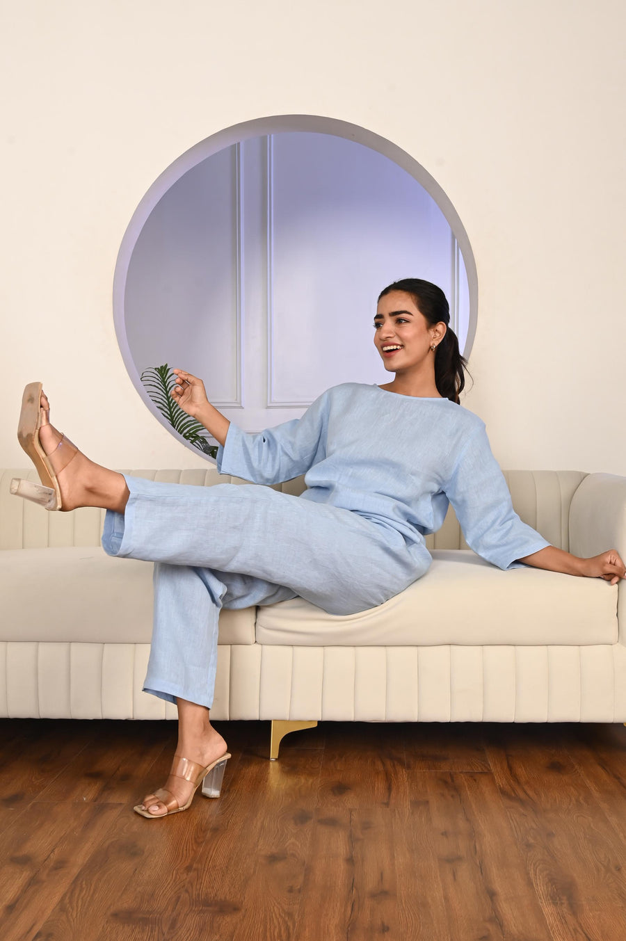 Washed Linen Tapered Pants: woman in Ice Blue linen top and trousers, seated on a sofa with leg raised
